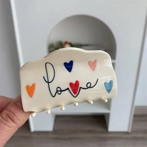 Detail van de crème haarklem van acetaat met kleurrijke hartjes en Love-belettering