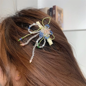Détail de la pince à cheveux fleurie en perles artisanales avec pompons bleus et roses