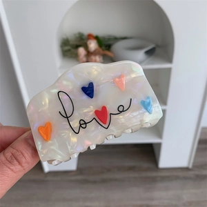 Detail van crème haarklem met kleurrijke hartjes en zwarte love-belettering op zij