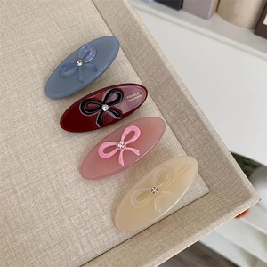 Close-up of four colorful acetate hair clips with bow designs and crystal centers