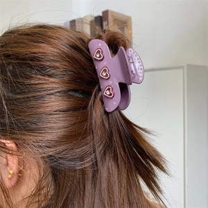 Detail einer lila Blumen-Haarklammer mit roten Strass-Herzmustern im Haar getragen