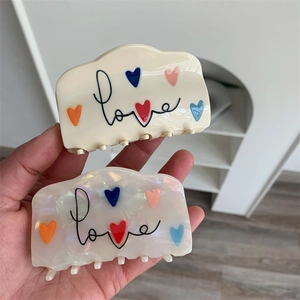 Detailopname van acetaat haarklemmen met hartjespatroon en love-tekst in diverse kleuren