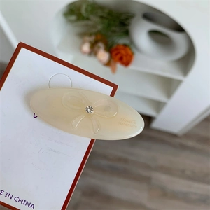 Close-up of cream-white acetate oval hair clip with embossed bow and small rhinestone