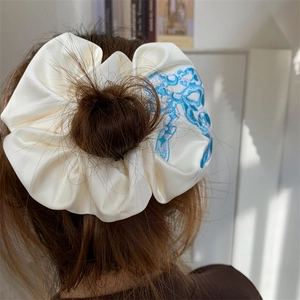 Detailed close-up of cream satin scrunchie with delicate floral embroidery on hair