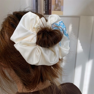 Detailed view of beige satin scrunchie with blue embroidery pattern on a ponytail