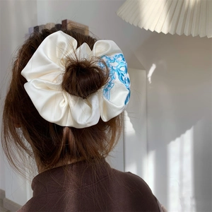 White satin scrunchie with blue embroidery shown in a bun hairstyle on high-quality fabric