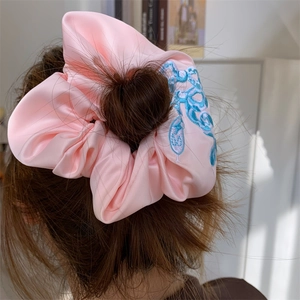 Pink satin scrunchie with blue embroidery on model hair with a minimalist interior background