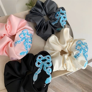 Detailed close-up of premium satin scrunchies featuring intricate blue snake embroidery