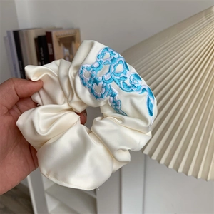 Close-up of beige satin scrunchie with detailed blue and cyan bow embroidery