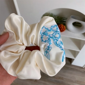 Close-up of ivory satin scrunchie with blue butterfly embroidery detail held in hand