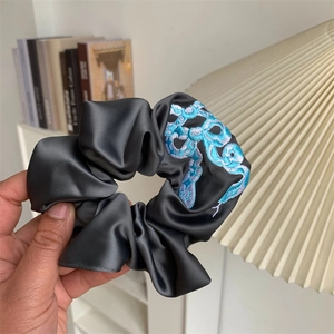 Close-up of dark grey satin scrunchie with colorful snake embroidery held in hand