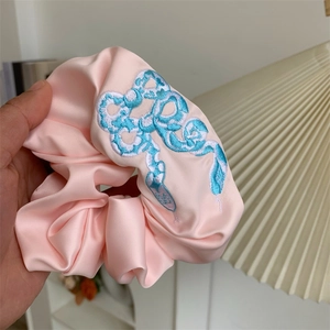 Detail of light pink satin scrunchie featuring elegant blue and white snake embroidery