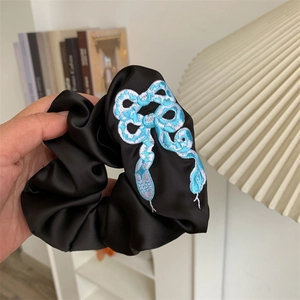 Close-up of black satin scrunchie with detailed blue and white snake embroidery