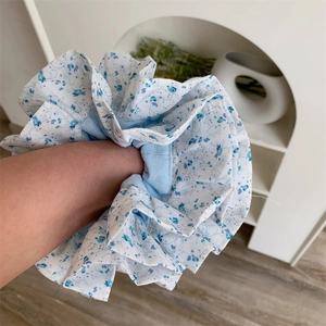 Détail d'un grand chouchou à fleurs bleues au poignet avec une texture plissée