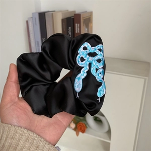 Detailed embroidery of blue and white snake patterns on a black satin scrunchie accessory