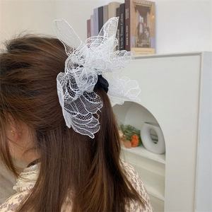Detail of a large white lace mesh flower hair tie on long brown hair in a French style
