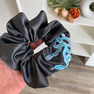 Close-up of a dark grey satin scrunchie with blue snake embroidery and silk-like sheen