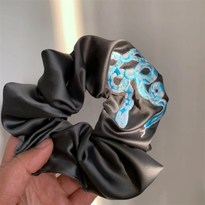 Detail of dark grey satin scrunchie with high-quality blue snake embroidery texture