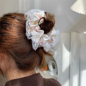 Detailed close-up of a cream satin floral scrunchie with lace trim worn on a bun
