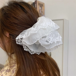 Close-up of white lace scrunchie with layered embroidery on brown wavy hair