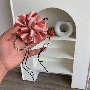 Détail du chouchou en satin rose avec tissu plissé élégant et longs rubans noirs
