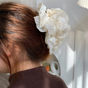 Detail of elegant cream lace ruffle hair scrunchie styled on a soft low ponytail