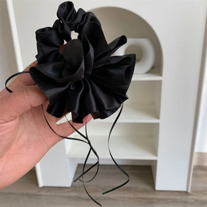 Détail d'un chouchou noir en satin avec rubans, montrant la texture soyeuse et brillante