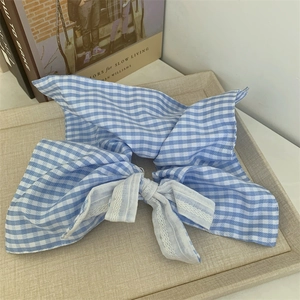 Blue and white gingham hair scrunchie with large bow and lace trim on a tray