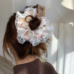 Detailed close-up of a large floral silk scrunchie with elegant white lace trim on a bun