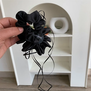 Détail d'un chouchou en satin noir avec de longs rubans et étiquette faite à la main