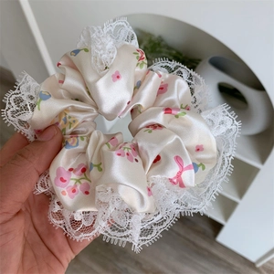 Close-up of a satin scrunchie featuring floral bow patterns and white lace trim detail