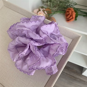 Elegant lavender ruffled silk scrunchie with detailed stitching on a textured display tray