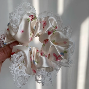 Detailed view of cream floral satin hair scrunchie with elegant white lace trim edge
