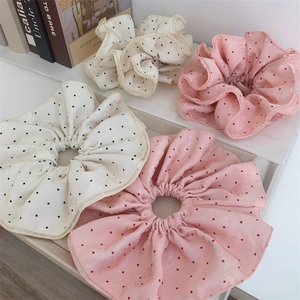 Detailed view of oversized polka dot hair scrunchies in pink and beige silk-like fabric