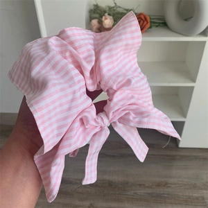 Detail showing hand holding a pink and white striped cotton scrunchie with a bow knot