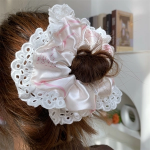 Detailed view of oversized pink silk scrunchie with white lace trim on hair bun
