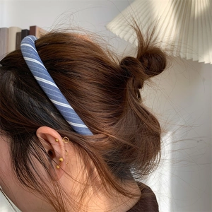Detail view of a blue striped headband paired with elegant golden stud earrings
