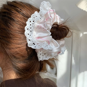 Close-up of a large pink silk scrunchie with white lace edges on a model's hair bun
