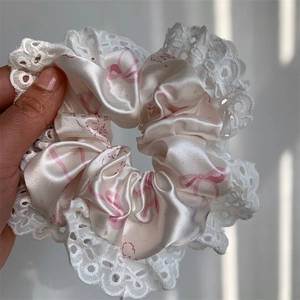 Close-up of pink satin scrunchie featuring bow patterns and delicate white eyelash lace