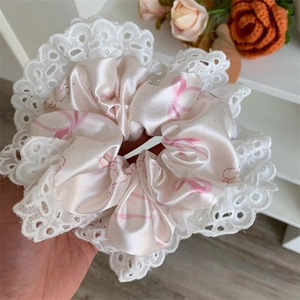 Close-up of silk pink hair scrunchie with bow prints and delicate white lace edges