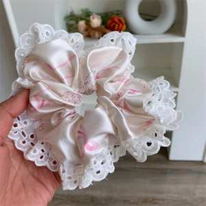 Detail view showing large pink satin hair scrunchie with lace trim and sweet ribbon print
