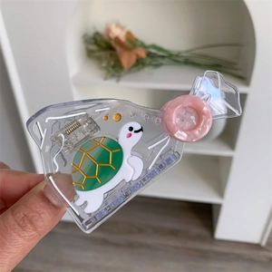 Detail of candy-shaped transparent acetate hair claw with a green turtle and marble button