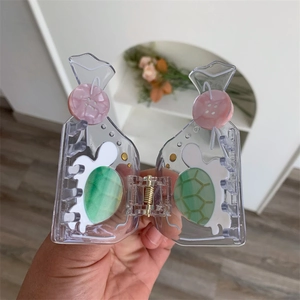 Detail of transparent acetate hair claw with green tortoise pattern and pink button decor
