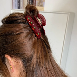 Detailansicht einer burgunderroten Haarklammer mit Kirsch-Strass-Mustern am Haar des Modells