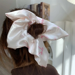 Detailed view of cream satin scrunchie with pink bow prints on a ponytail