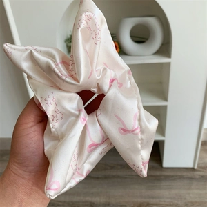 Detail of pink satin scrunchie with bow patterns and lace trim shown held by hand