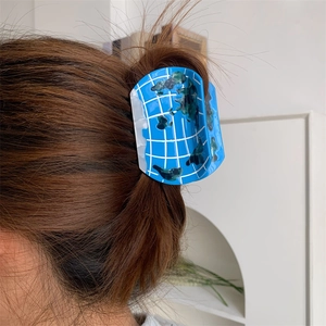 Blue acetate hair claw clip with globe map design shown on a brunette model