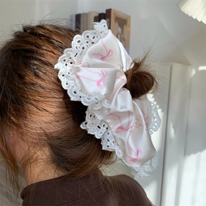 Detail of a large white satin bow hair tie with pink ribbon patterns and lace edges