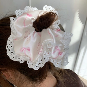 Detail of white silk scrunchie with pink bow prints and delicate lace embroidery edge