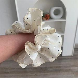 Detailed view of a large beige satin scrunchie with black polka dots worn on wrist